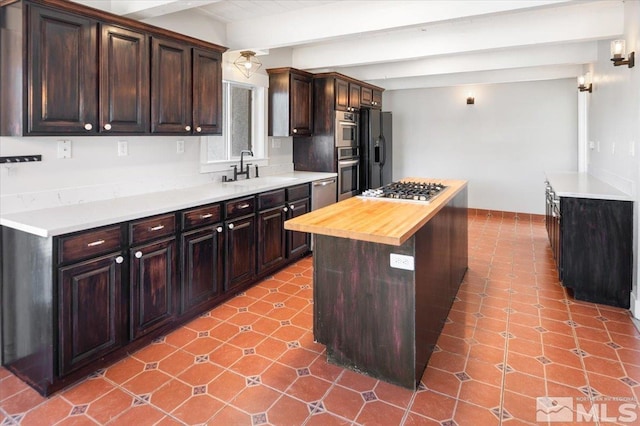 kitchen featuring beam ceiling, a sink, a kitchen island, appliances with stainless steel finishes, and dark brown cabinets