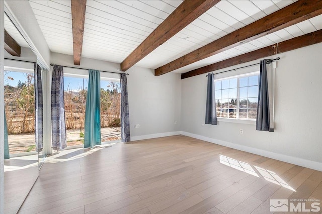 unfurnished room with beamed ceiling, wood finished floors, baseboards, and a wealth of natural light