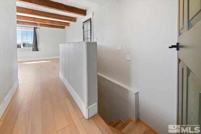 corridor featuring beam ceiling, an upstairs landing, baseboards, and hardwood / wood-style floors