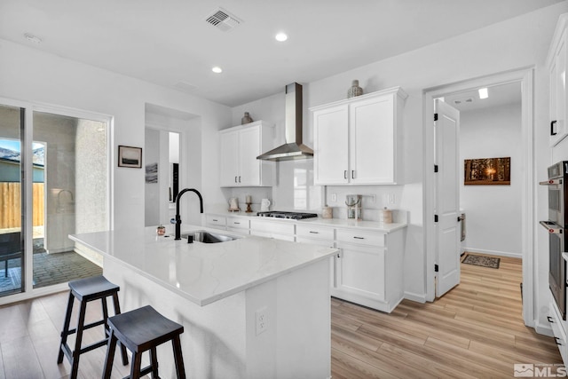 kitchen with a breakfast bar, light wood-style flooring, a sink, gas stovetop, and wall chimney range hood