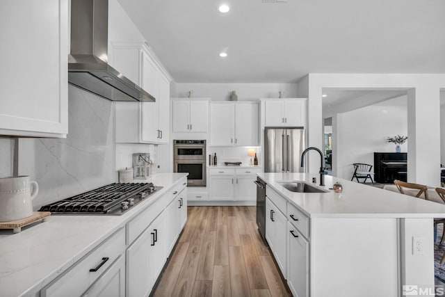 kitchen featuring light countertops, wall chimney range hood, appliances with stainless steel finishes, and a sink