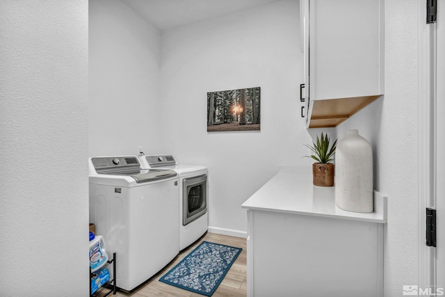 washroom featuring washer and dryer, cabinet space, baseboards, and light wood finished floors