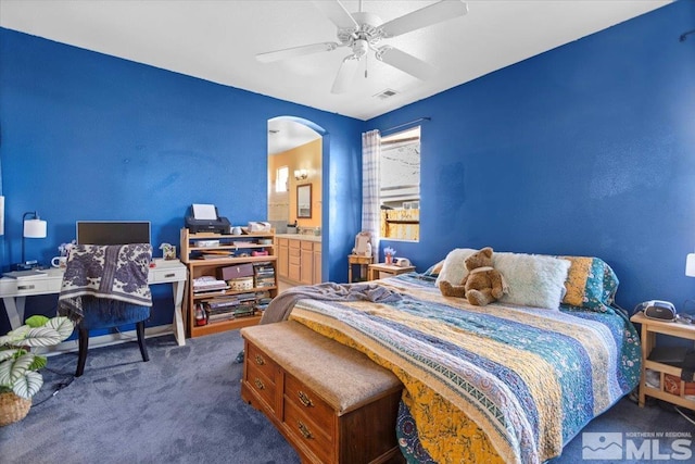 bedroom with visible vents, carpet flooring, ensuite bathroom, arched walkways, and a ceiling fan