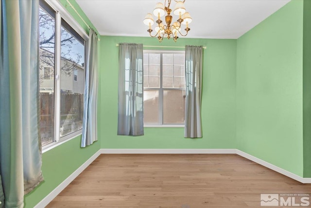 unfurnished dining area featuring a chandelier, baseboards, and wood finished floors