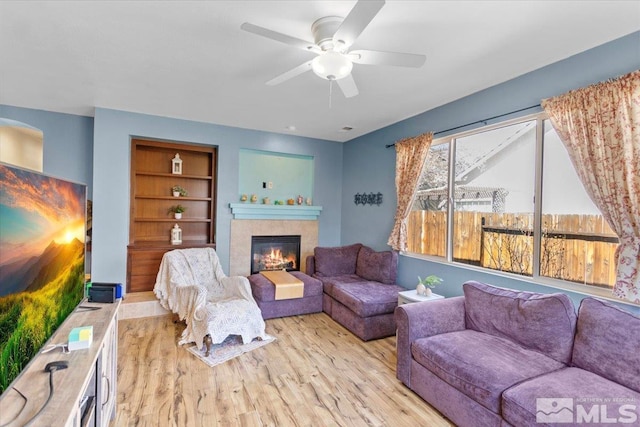 living room with built in shelves, ceiling fan, a fireplace, and light wood finished floors