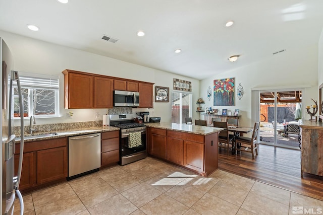 kitchen featuring visible vents, a sink, stainless steel appliances, a peninsula, and brown cabinetry