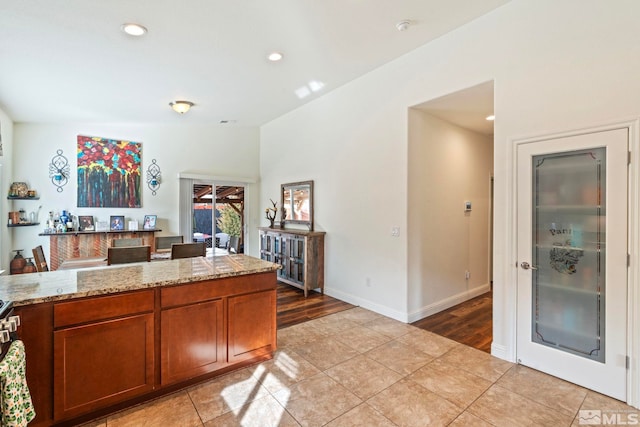 kitchen featuring baseboards, light stone countertops, light tile patterned floors, recessed lighting, and brown cabinets