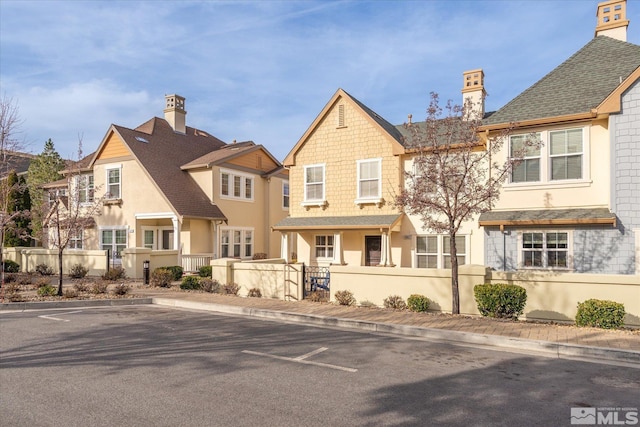 view of front facade featuring a fenced front yard, stucco siding, a chimney, and roof with shingles