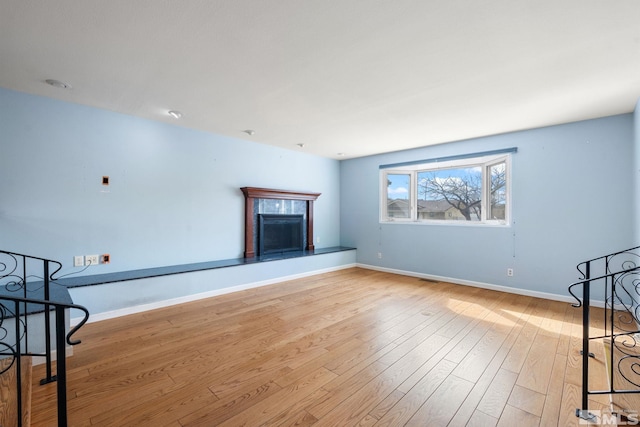 living area with baseboards, light wood-style floors, and a fireplace with raised hearth