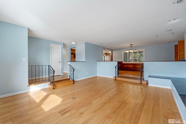 unfurnished living room with light wood-style flooring, baseboards, and a chandelier