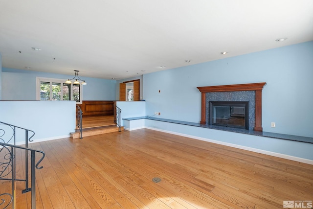 unfurnished living room featuring baseboards, an inviting chandelier, wood finished floors, and a tile fireplace