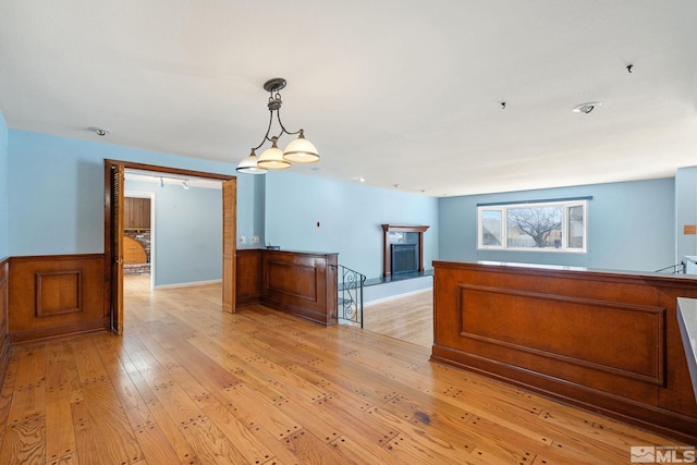 kitchen featuring a wainscoted wall, pendant lighting, a fireplace with raised hearth, and light wood finished floors