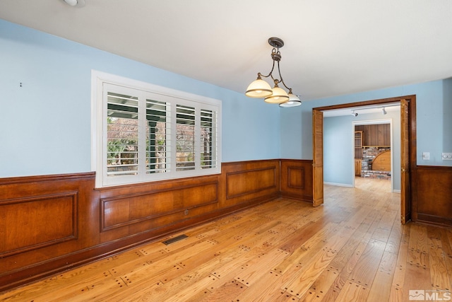 unfurnished room with visible vents, a wainscoted wall, and light wood finished floors