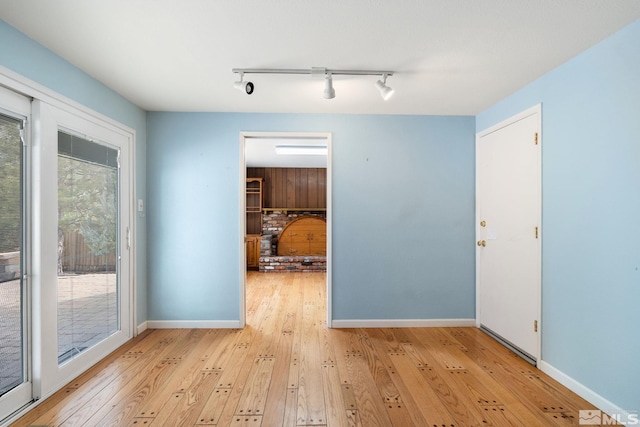 empty room with baseboards, track lighting, and light wood finished floors