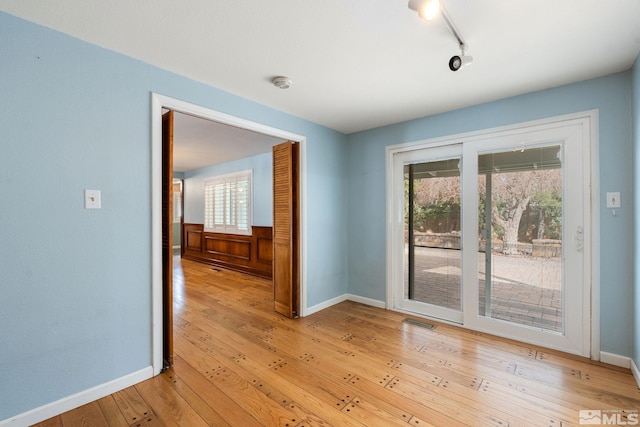 spare room with rail lighting, baseboards, light wood-type flooring, and a wealth of natural light