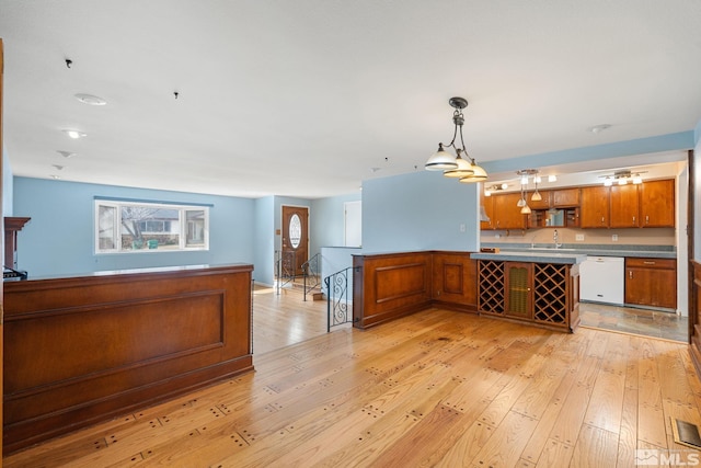 kitchen with decorative light fixtures, open shelves, light wood-style floors, brown cabinetry, and white dishwasher