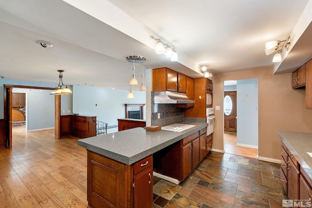 kitchen with under cabinet range hood, white oven, baseboards, and decorative backsplash