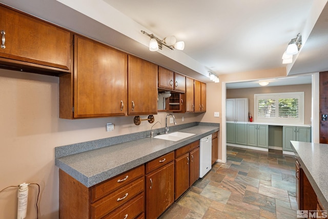 kitchen with baseboards, brown cabinets, white dishwasher, stone finish floor, and a sink