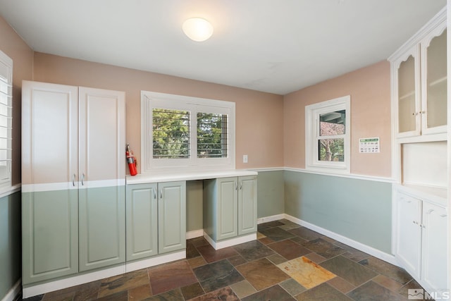 kitchen with glass insert cabinets, baseboards, stone tile floors, and light countertops