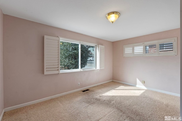 empty room with carpet, visible vents, a wealth of natural light, and baseboards