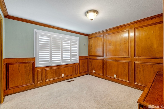 carpeted empty room featuring crown molding, visible vents, and wainscoting