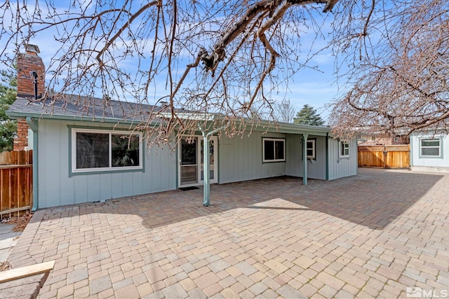 rear view of house featuring a chimney, a patio, and fence