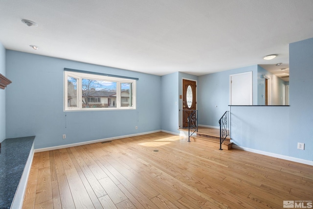 unfurnished living room with hardwood / wood-style floors and baseboards