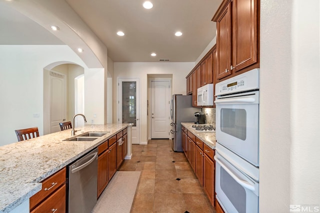 kitchen featuring visible vents, light stone counters, decorative backsplash, white appliances, and a sink