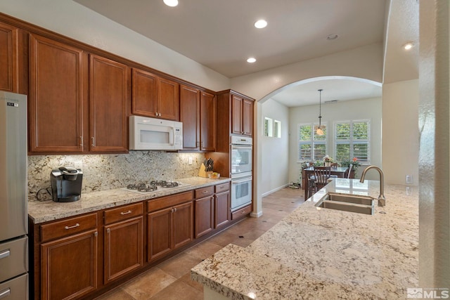 kitchen featuring light stone countertops, decorative backsplash, arched walkways, white appliances, and a sink