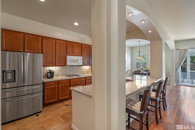 kitchen with a breakfast bar, backsplash, white appliances, brown cabinetry, and light stone countertops