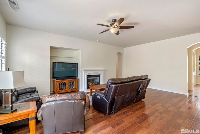 living room featuring a ceiling fan, wood finished floors, baseboards, arched walkways, and a glass covered fireplace