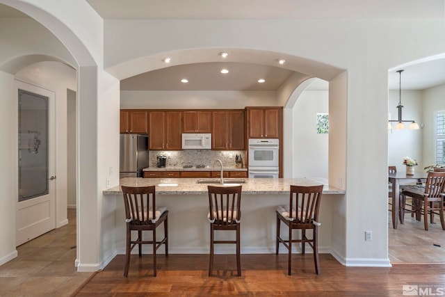 kitchen featuring tasteful backsplash, brown cabinets, a peninsula, and white appliances