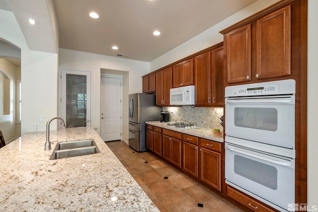 kitchen with tasteful backsplash, light stone counters, recessed lighting, white appliances, and a sink