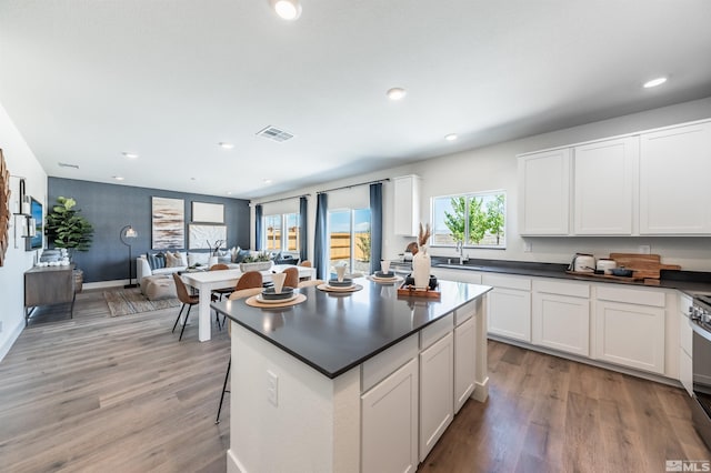 kitchen featuring visible vents, a sink, white cabinets, dark countertops, and light wood-type flooring