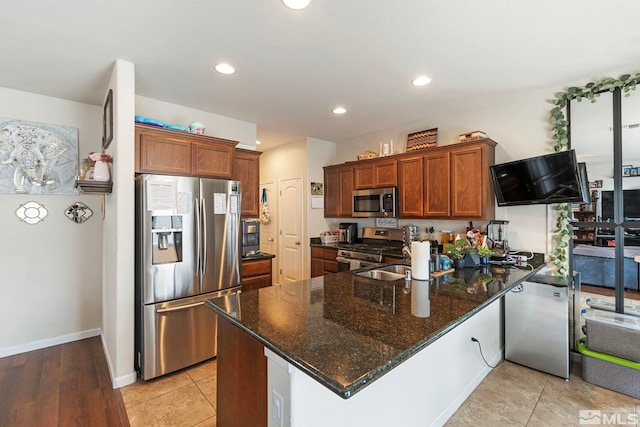 kitchen with dark stone countertops, a peninsula, recessed lighting, appliances with stainless steel finishes, and brown cabinets