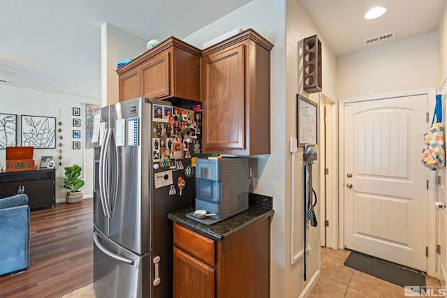 kitchen with brown cabinetry, baseboards, visible vents, dark stone counters, and stainless steel refrigerator with ice dispenser