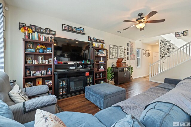 living room with a glass covered fireplace, stairs, wood finished floors, and visible vents