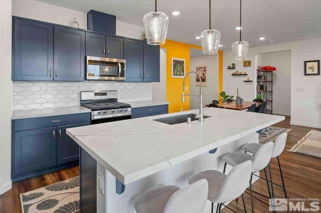 kitchen with tasteful backsplash, a sink, an island with sink, appliances with stainless steel finishes, and dark wood-style flooring