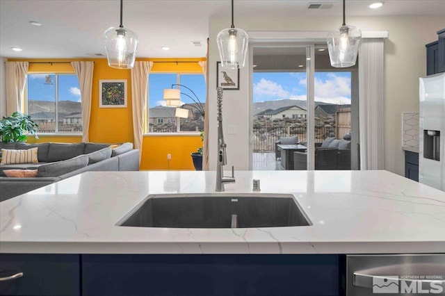 kitchen featuring a kitchen island with sink, light stone counters, open floor plan, and pendant lighting