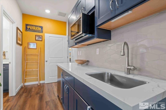 kitchen with stainless steel microwave, light stone counters, decorative backsplash, dark wood-style floors, and a sink