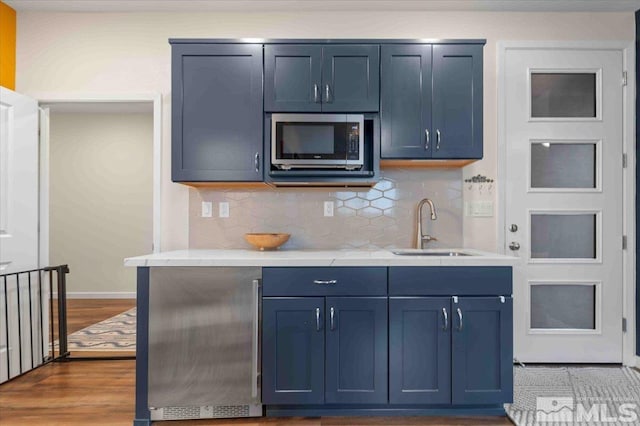 kitchen with tasteful backsplash, stainless steel microwave, light countertops, wood finished floors, and a sink