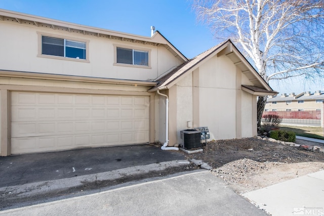 view of front of house with central AC, an attached garage, driveway, and stucco siding