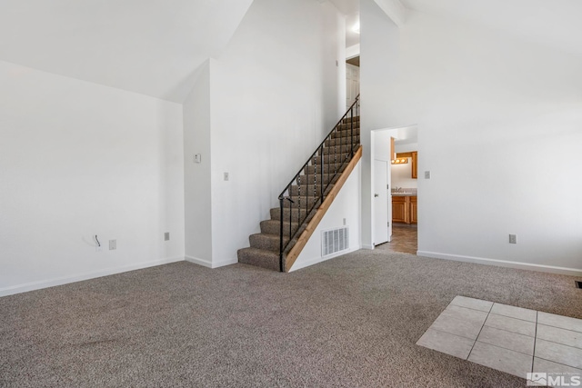 unfurnished living room with high vaulted ceiling, visible vents, carpet, and stairs