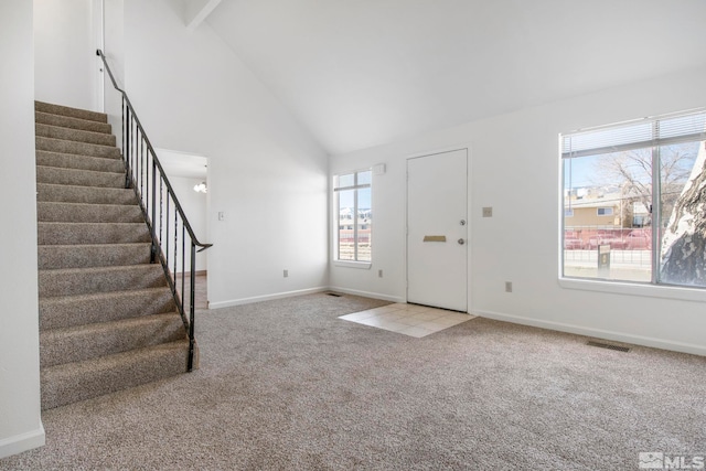 carpeted foyer entrance with visible vents, high vaulted ceiling, stairs, and baseboards