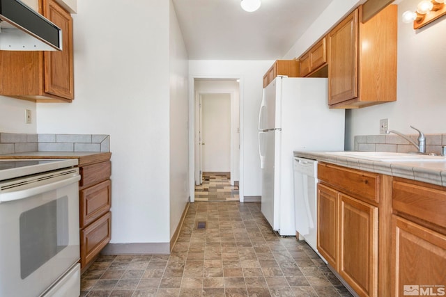 kitchen featuring ventilation hood, tile counters, stone finish floor, white appliances, and a sink