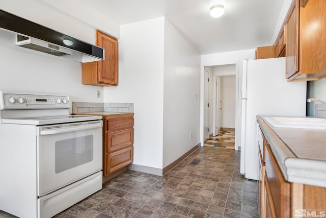 kitchen with under cabinet range hood, baseboards, white appliances, and stone finish floor