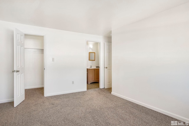 unfurnished bedroom with a walk in closet, a closet, connected bathroom, baseboards, and light colored carpet