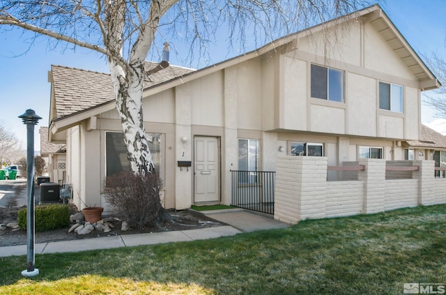 view of front facade featuring stucco siding, a front lawn, fence, roof with shingles, and central AC unit