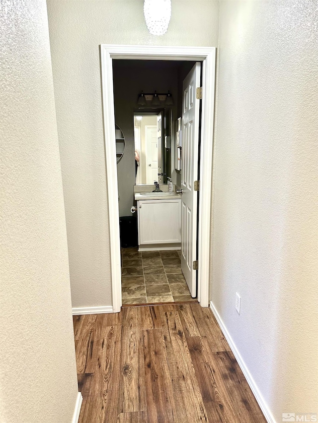 hallway with a sink, baseboards, and dark wood-style floors