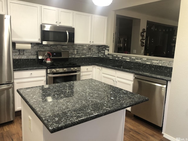 kitchen with dark stone countertops, dark wood finished floors, stainless steel appliances, white cabinetry, and tasteful backsplash